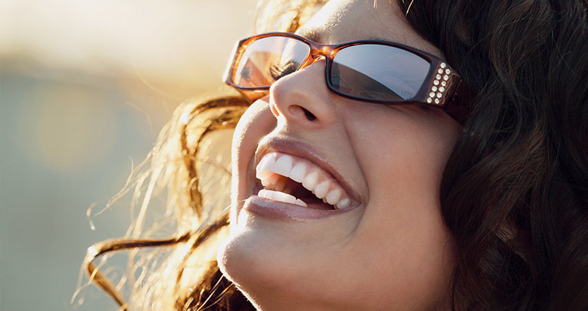 caucasian woman brunette head tilted back sunshine white smile sunglasses