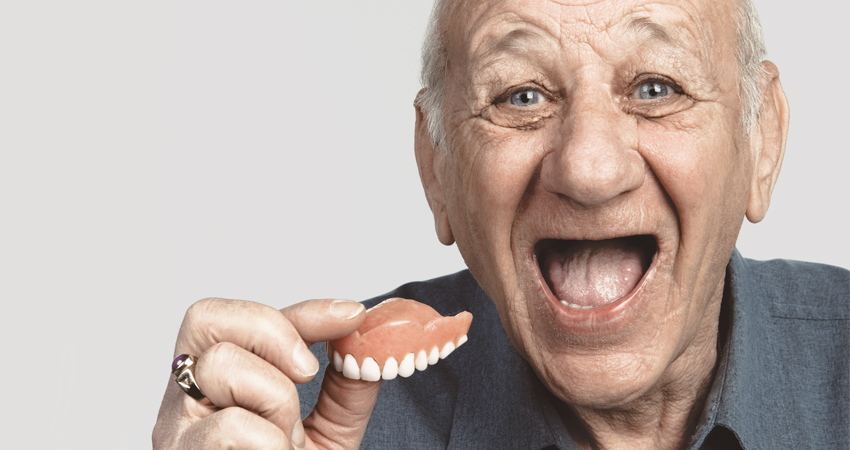 Senior holds his dentures and smiles